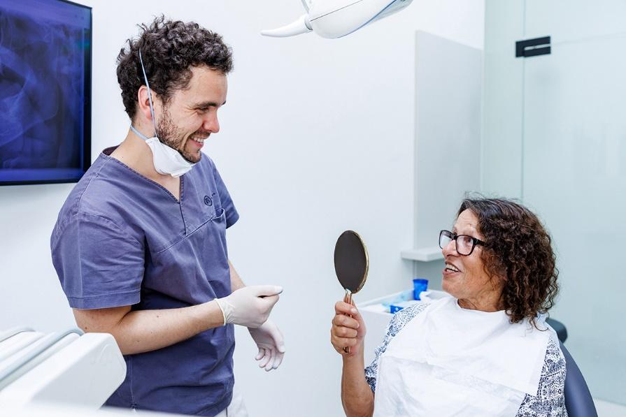 Dr. Artúr Varajti, Zahnarzt und Oralchirurg bei Artdent in Budapest, im Gespräch mit einer zufriedenen Patientin, die ihre neue Klickprothese im Handspiegel betrachtet