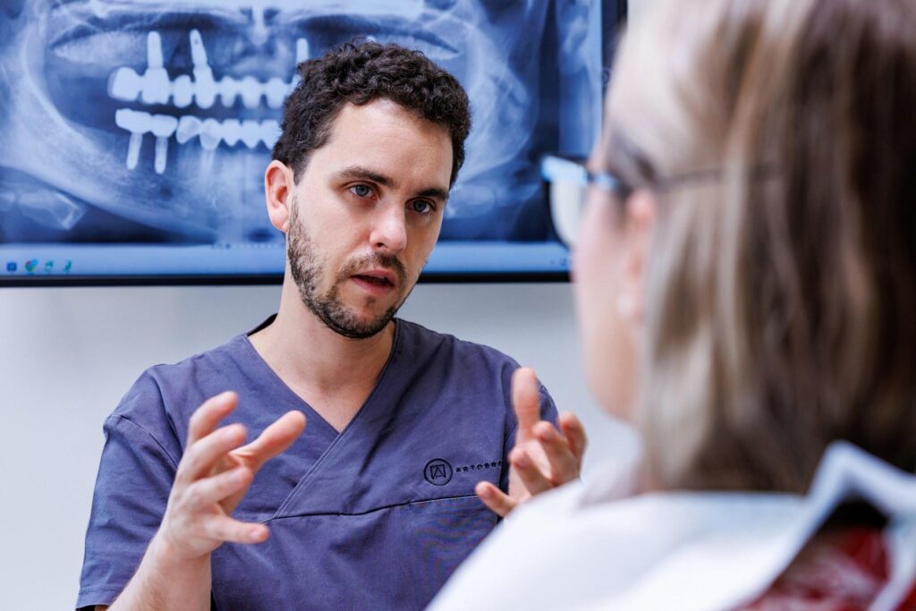 Zahnarzt der ArtDent Zahnklinik in Budapest erklärt einer Patientin anhand des Röntgenbildes den Behandlungsplan mit Zahnimplantaten