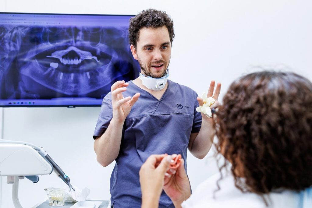 Zahnarzt der Artdent Zahnklinik in Budapest erklärt einer Patientin anhand des Panorama-Röntgenbildes und eines Zahnmodells die geplante Versorgung.